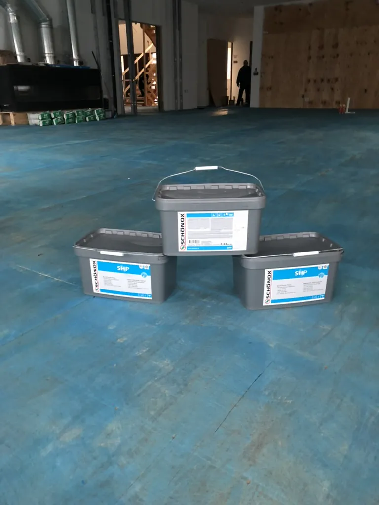 1 Wood Floors  Buckets of specialized blue bonding primer sitting on a bare subfloor, utilized by 1 Wood Floors to ensure permanent adhesion of self-leveling underlayment in Northville, MI. Installed by 1 Wood Floors, Livonia, MI
